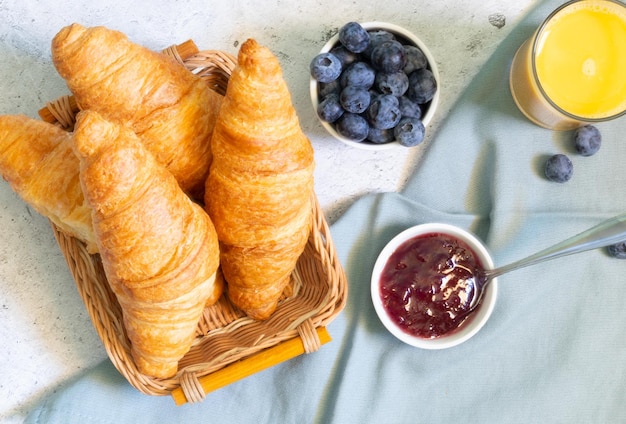 Mermelada de bayas croissants y jugo sobre fondo claro con textiles azul claro