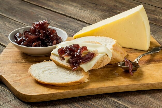 Mermelada de cebolla en un platillo, pan blanco y queso en una tabla para cortar. Enfoque selectivo.