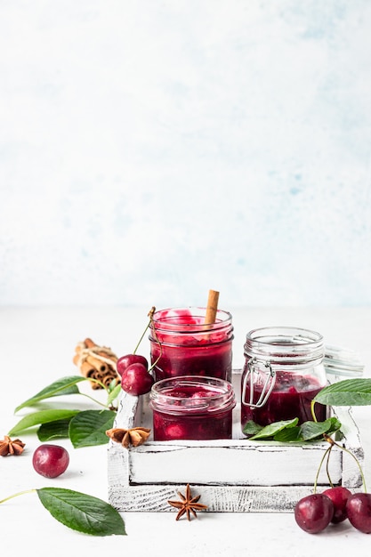 Mermelada de cereza casera con especias (canela, anís) con cerezas frescas en los frascos sobre una piedra clara