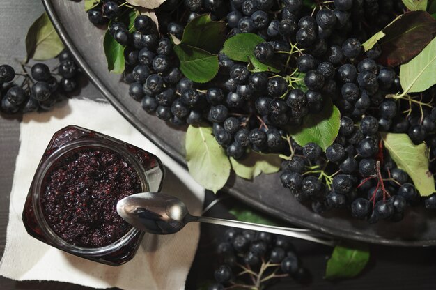 Mermelada de chokeberries negros y sus bayas en la mesa oscura.