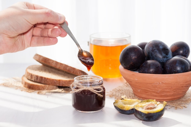 Mermelada de ciruela casera dulce y frutas sobre una mesa blanca en un día soleado.