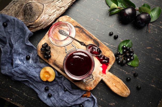 Mermelada de ciruela recién hecha en un frasco y frutas en una mesa con cortinas.