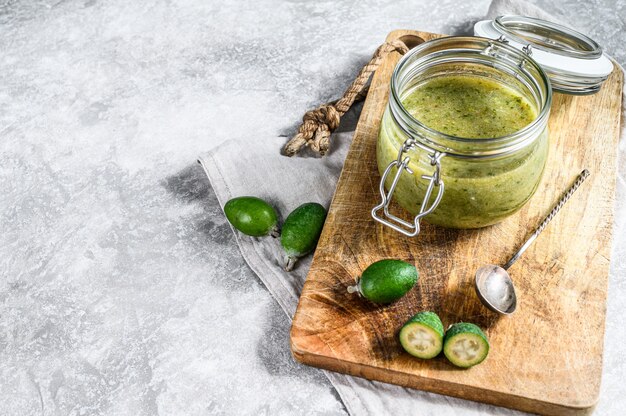 Mermelada de feijoa verde en una tabla de cortar de madera en un frasco de vidrio. fondo gris vista superior. espacio para texto.