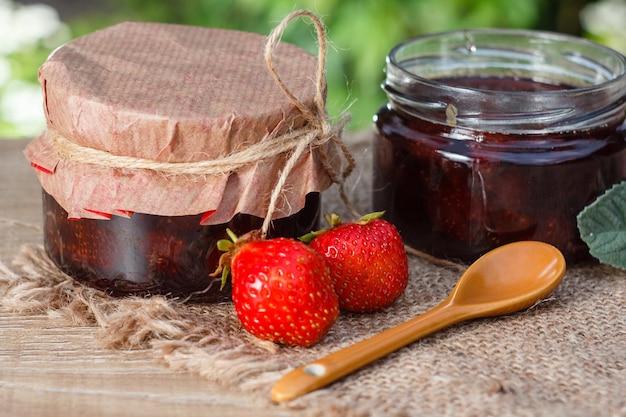 Mermelada de fresa casera tradicional en frascos con fresas frescas sobre mesa de madera