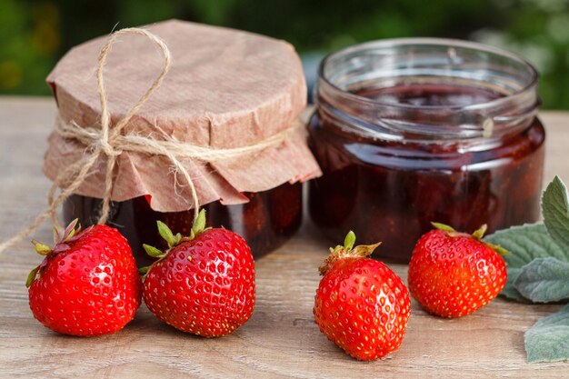 Mermelada de fresa casera tradicional en frascos con fresas frescas sobre mesa de madera