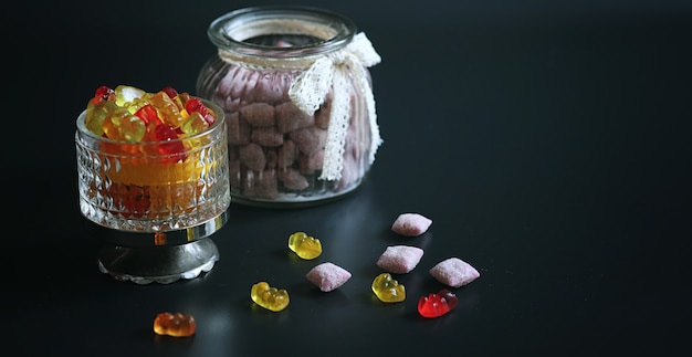 Mermelada en un jarrón sobre la mesa. Dulces en un cuenco sobre un fondo negro. Caramelos de gelatina multicolor para niños.