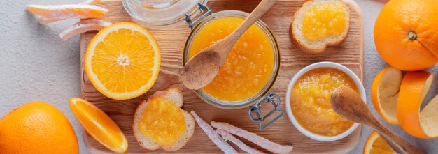 Mermelada de naranja en un frasco, frutas de naranja confitadas, pan, naranja fresca sobre una tabla de madera.