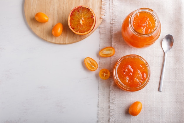 Mermelada de naranja y kumquat en un frasco de vidrio con frutas frescas en blanco
