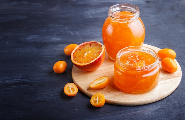 Mermelada de naranja y kumquat en un frasco de vidrio con frutas frescas en madera negra