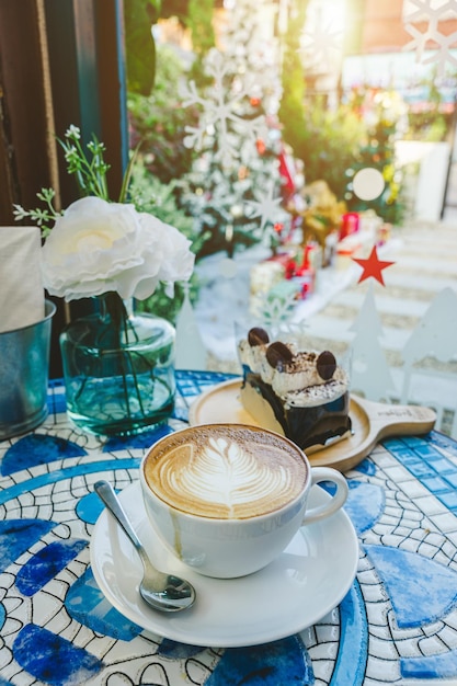 Merry xmasHeißer Kaffee Latte mit Latte-Art-Milchschaum im Becher und hausgemachter Schokoladenkuchen mit Weihnachtsdekoren und Weihnachtsbaumkugeln auf dem Schreibtisch mit Marmorboden Feiern von frohen Weihnachten und Neujahr