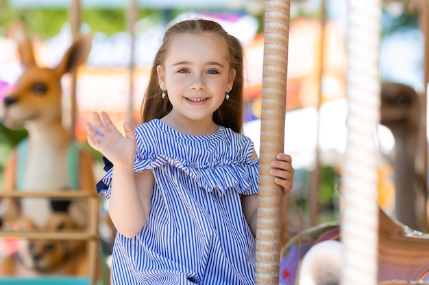 Merrygoround linda niña con vestido azul jugando en el carrusel en el parque de diversiones