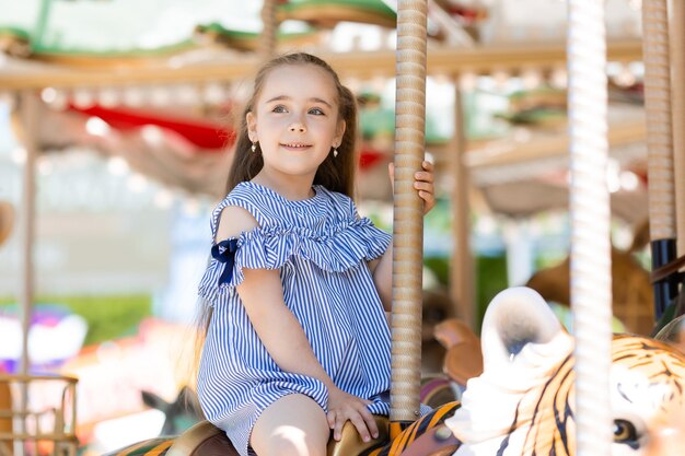 Merrygoround süßes kleines Mädchen im blauen Kleid, das im Vergnügungspark auf dem Karussell spielt