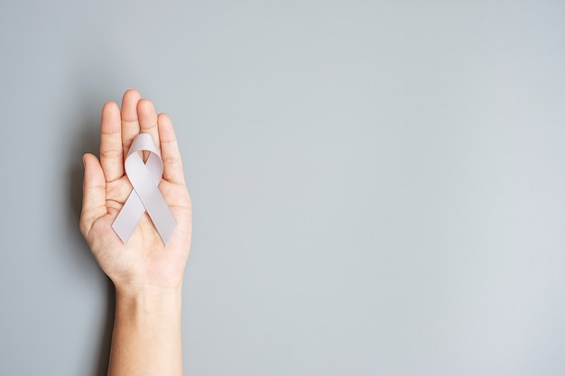 Mes de concientización sobre el cáncer de cerebro, mano de mujer sosteniendo una cinta de color gris para apoyar a las personas que viven. Concepto de salud y día mundial contra el cáncer