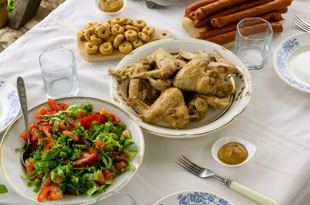 Mesa con alitas de pollo fritas, ensalada de tomate y bocadillos.