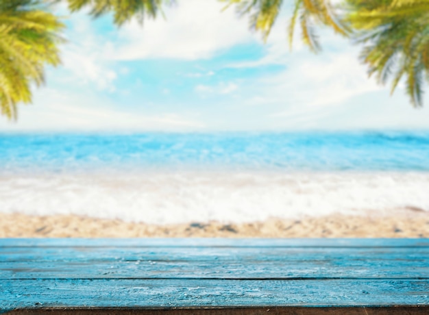 Mesa azul vacía contra un espacio de playa con el mar y las palmeras (Mock Up)