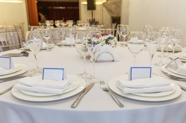 Mesa de banquete elegantemente servida con tarjetas personalizadas. Hermosas flores, platos vacíos sobre un mantel blanco.