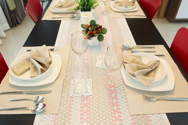 Mesa bellamente decorada con platos blancos, vasos de cristal, servilletas de lino, cuchara, cuchillo y tenedor sobre manteles lujosos