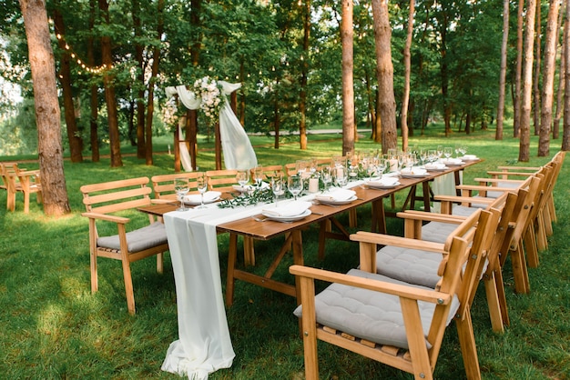 Mesa de boda con decoración rústica en el bosque. Platos y rama verde con velas sobre la mesa. Decoración verde.