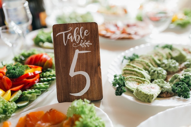 Foto mesa de boda decorada y numerada con comida, bebida, electrodomésticos y flores.