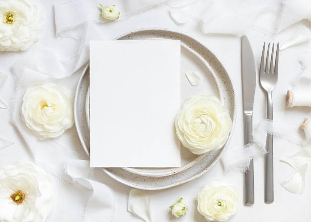 Mesa de boda con tarjeta cerca de rosas color crema y maqueta de vista superior de cintas de seda blanca