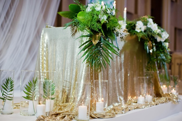 Mesa de bodas con adornos dorados hojas verdes tropicales y velas encendidas en jarrones de vidrio