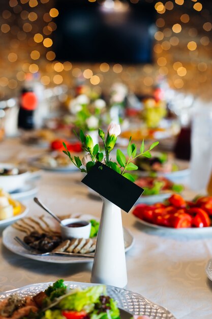 Una mesa de bodas con muchos platos deliciosos y un florero con una tarjeta de visita.