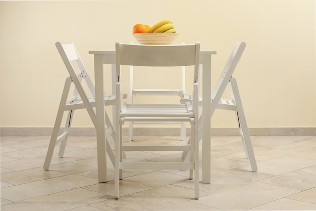 Foto mesa branca com frutas e cadeiras dobráveis na cozinha