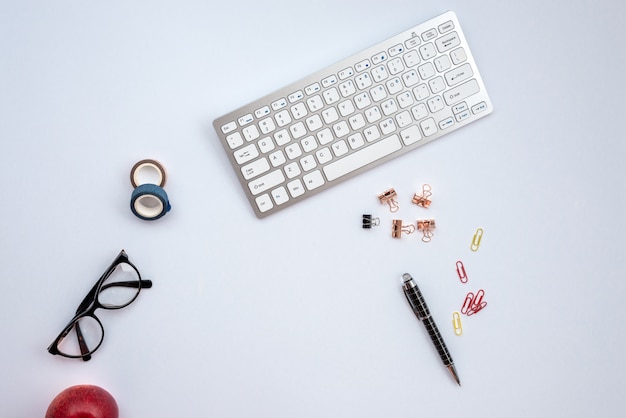 Mesa branca com teclado, caneta, óculos e acessórios