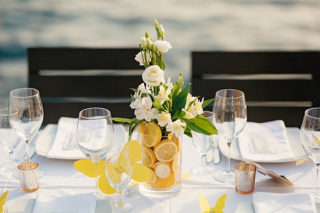 Mesa de cena de boda recepción baño transparente de cristal con rodajas de limones y un ramo de blanco