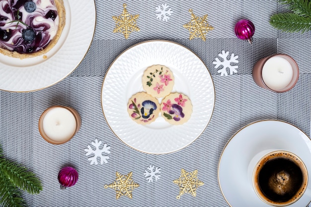 Mesa de la cena de Navidad con hermosas galletas de flores comestibles y una tarta de queso con arándanos