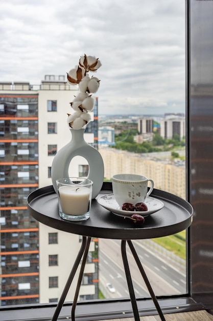 Mesa de centro con una taza, una vela, una cereza y un jarrón con una rama de algodón en el fondo de