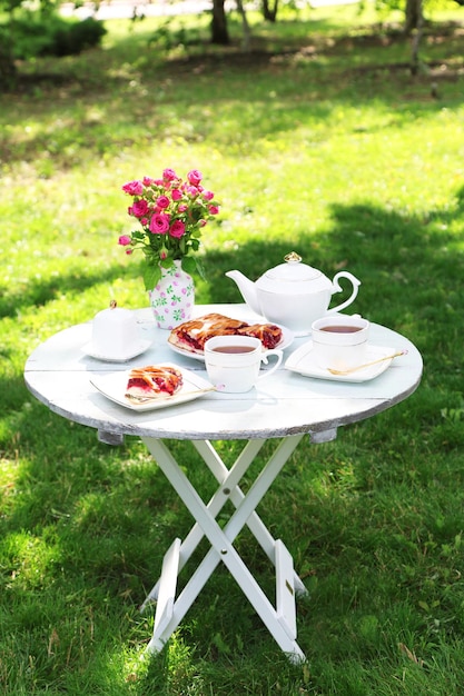 Mesa de centro con tazas de té y sabroso pastel en el jardín