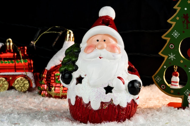 Mesa coberta com flocos de neve com decorações de Natal. Papai Noel, árvore de Natal com luzes e bolas vermelhas e douradas. Foco seletivo.