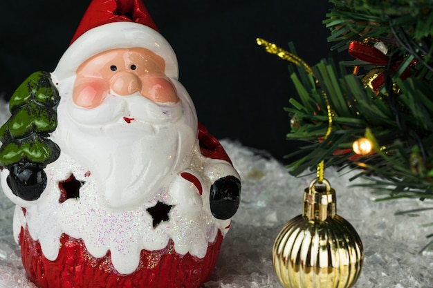 Mesa coberta com flocos de neve com decorações de Natal. Papai Noel, árvore de Natal com luzes e bolas vermelhas e douradas. Foco seletivo.