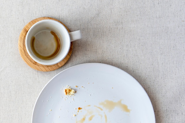 Mesa coberta por toalha de mesa com xícara de café para expresso, prato com migalhas de sobremesa, vista de cima, disposição plana