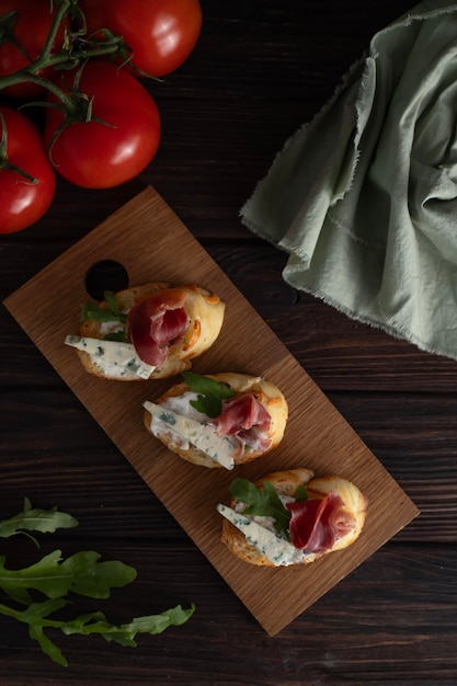 En la mesa de la cocina hay una tabla con bruschetta fresca con jamón y queso junto con tomates y g