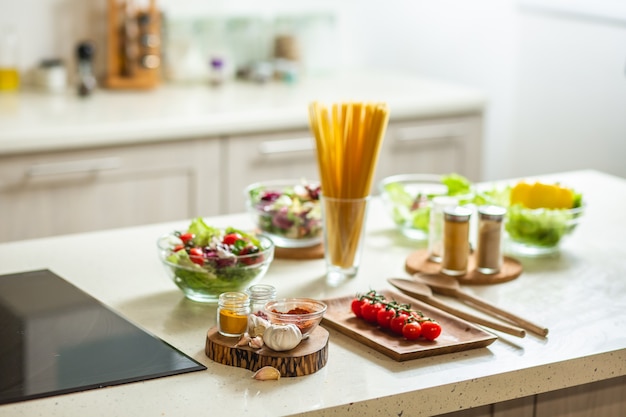 Mesa de cocina de piedra blanca con cuencos de ensaladas, especias y verduras