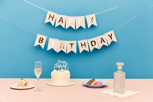 Mesa com delicioso bolo de champanhe e doces contra fundo azul com cartas de feliz aniversário