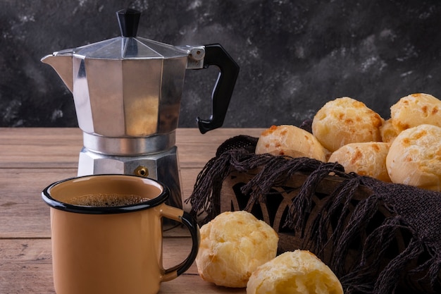 Mesa com deliciosos pães de queijo, uma xícara de café e uma cafeteira tradicional.