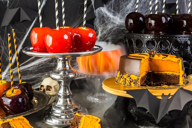 Mesa com maçãs doces coloridas e bolo para festa de Halloween.