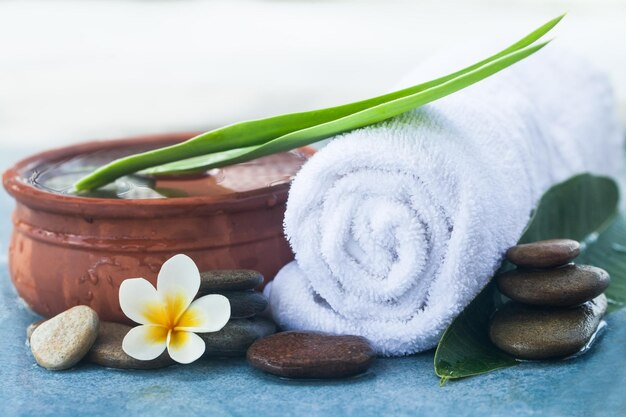 Mesa com objetos de spa e pedras de flores tropicais para tratamento de massagem em fundo azul