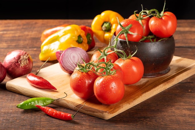 Mesa com pimentão vermelho e amarelo pimentão cebola e alho e tomate sobre foco seletivo de fundo preto de madeira rústica