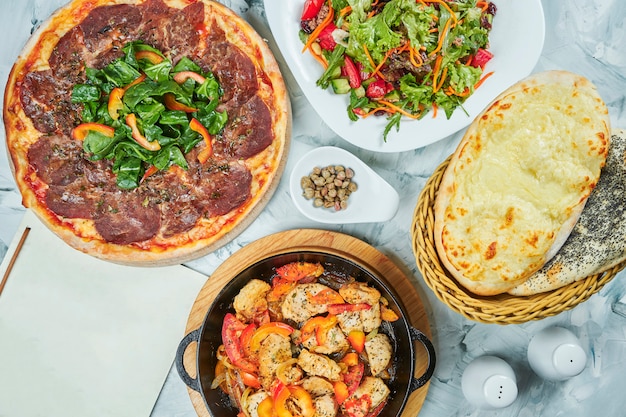 Mesa com planty de alimentos para o almoço, salada saudável, pizza com vitello tonatto vitela e carne frango pan com tomate. Mesa de comida plana