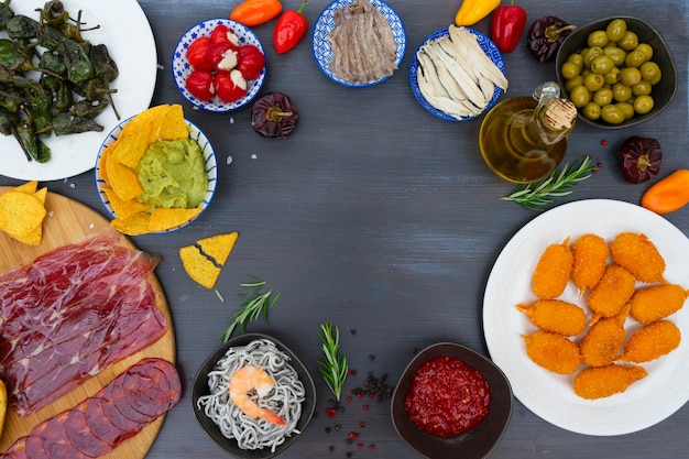 Foto mesa com tapas espanholas - anchovas com pimentos padron, jamon, croquetes, guacamole