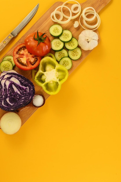 Mesa com tomate, pepino, repolho, cebola, alho, faca, sobre fundo amarelo, vista superior