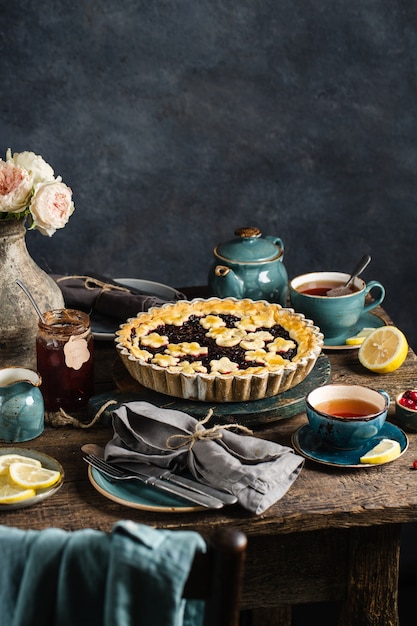 Mesa com torta quente de frutas vermelhas, xícaras quentes com chá de limão, geléia e flores