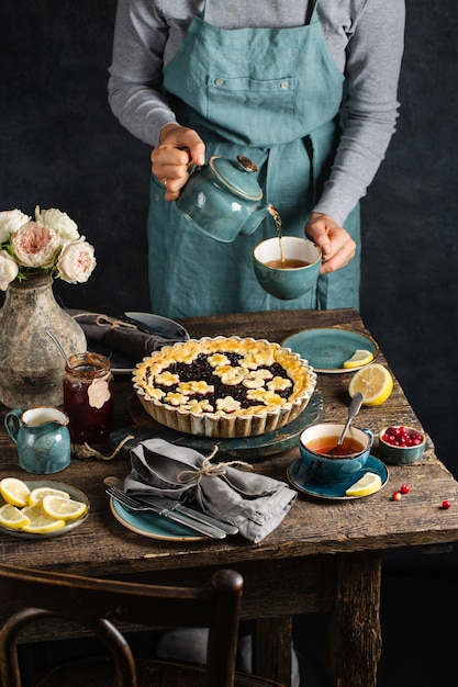 Mesa com torta quente de frutas vermelhas, xícaras quentes com chá de limão, geléia e flores