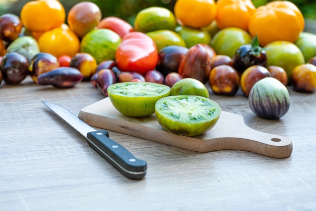 Mesa com uma tábua de cortar com tomates fatiados e tomates de cores diferentes ao fundo