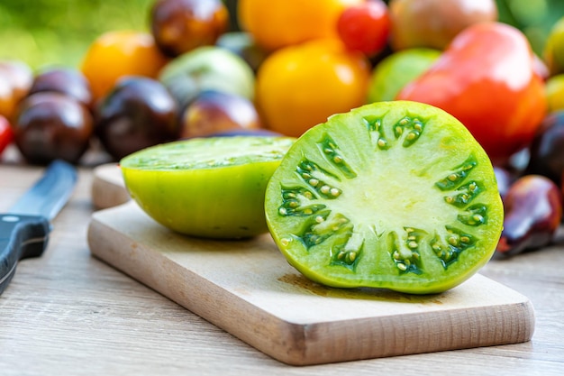 Mesa com uma tábua de cortar com tomates fatiados e tomates de cores diferentes ao fundo