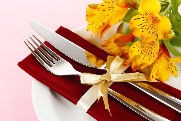 Mesa de comedor festiva con flores sobre fondo rosa